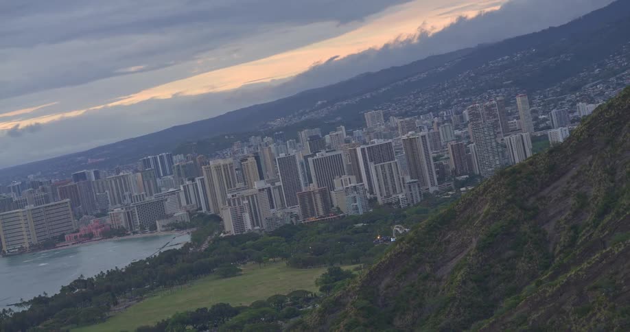 A Dutch angle shot from a high vantage point above Waikiki, Honolulu slowly levels out to reveal the city skyline and coastline at dusk
