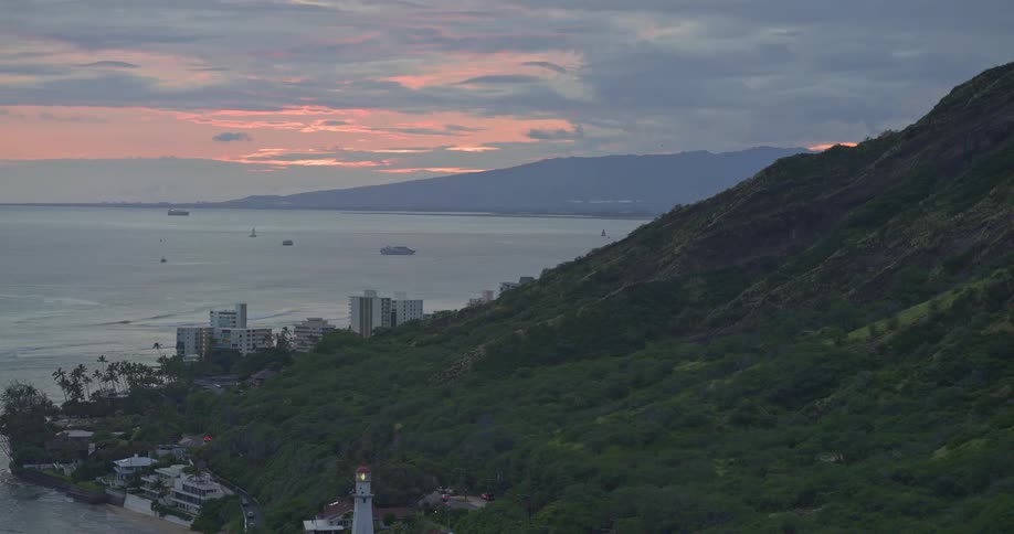 A beautiful aerial view rises over the Diamond Head Lighthouse on the coast of Oahu, Hawaii, as the sun sets over the ocean