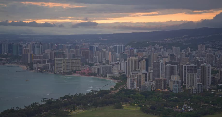 A beautiful aerial zoom-out shot reveals the stunning Waikiki skyline and coastline in Honolulu, Hawaii, at sunset