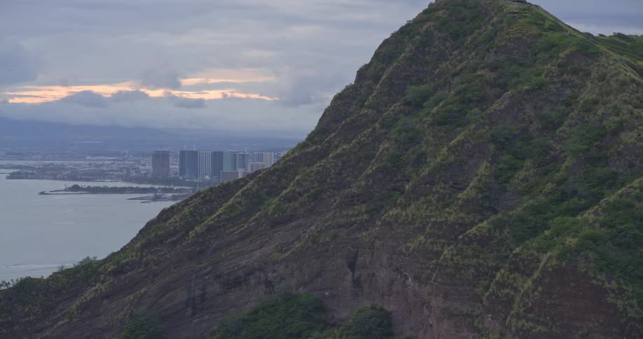 Aerial view panning left from Diamond Head crater reveals the Honolulu city skyline along the coast at dusk