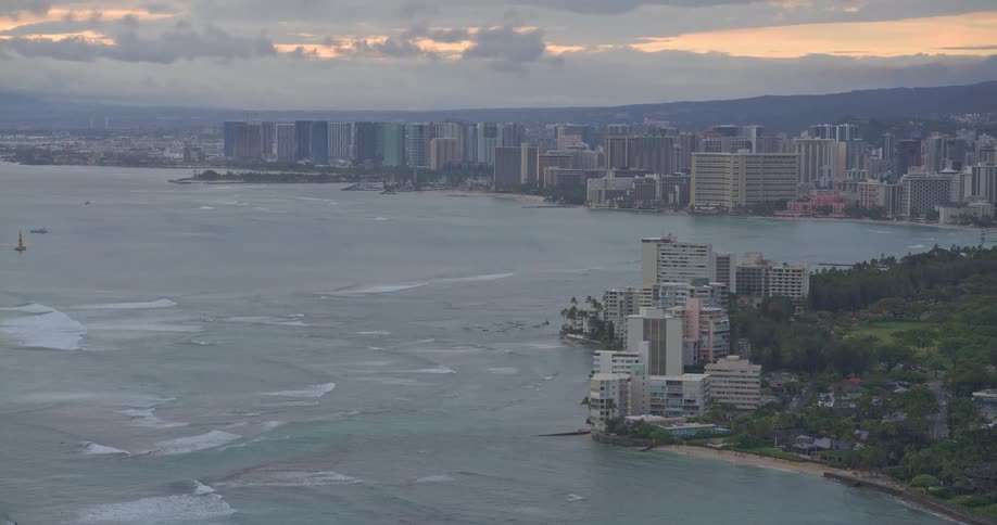 A wide panoramic zoom-out of the Honolulu skyline and Waikiki coast during a cloudy and atmospheric sunrise
