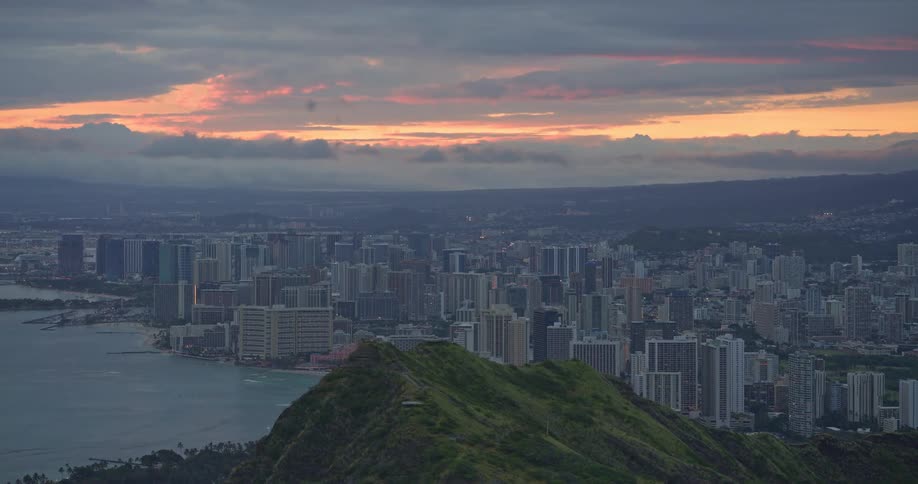 A stunning aerial view from a mountain peak reveals the Honolulu city skyline and Waikiki beach during a beautiful sunrise