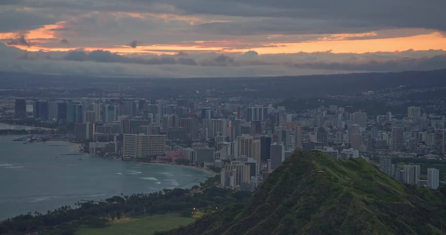A dramatic aerial shot reveals the lush Diamond Head crater overlooking the Waikiki skyline and Honolulu at sunset