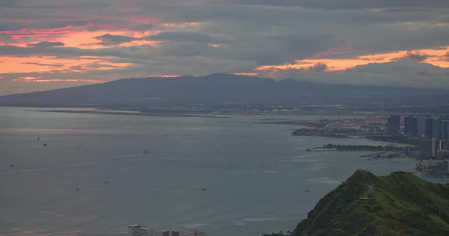An expansive view of the Hawaiian coastline and a cityscape from a high vantage point during a colorful sunset