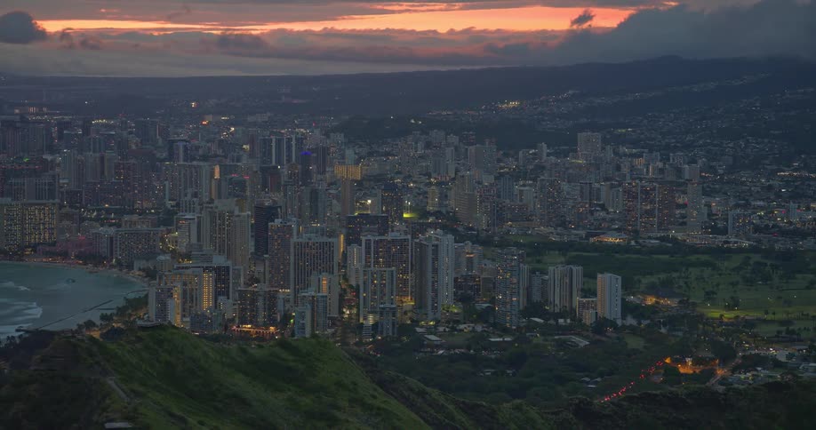 An elevated view of the Waikiki skyline as city lights begin to twinkle against a dramatic twilight sky in Honolulu, Hawaii