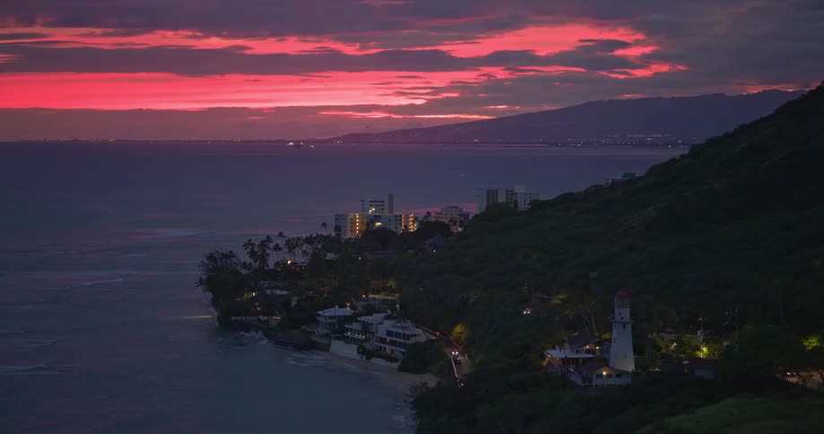 Stunning aerial view of a Hawaiian coastline at dusk, revealing a lighthouse under a dramatic pink and purple sunset sky