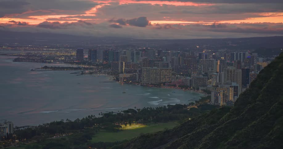 Stunning twilight aerial view over Honolulu and Waikiki Beach, with city lights beginning to sparkle as the camera pulls back to reveal the iconic Diamond Head crater