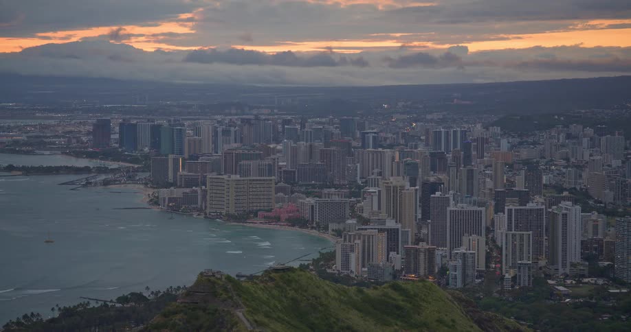 A scenic high-angle view captures the Waikiki skyline in Honolulu, Hawaii, transitioning from a cloudy sunset to twilight
