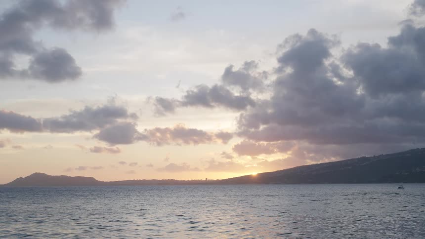 A serene sunset over the ocean with a cloudy sky and distant islands on the horizon