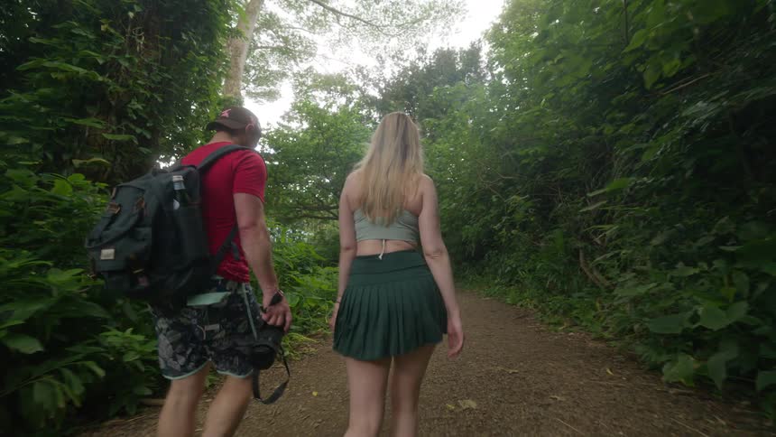 A young couple walks in slow motion down a scenic path through a lush tropical forest