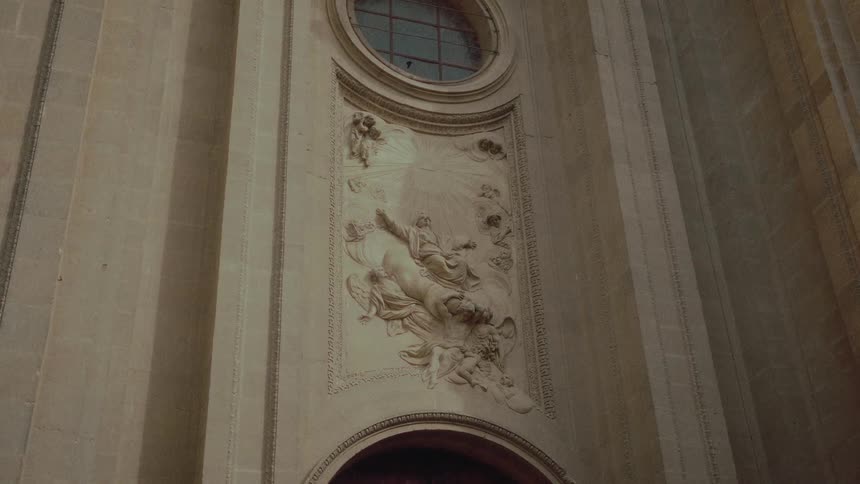 An ornate religious bas-relief sculpture depicting an ascension scene is displayed on the interior stone wall of a historic church