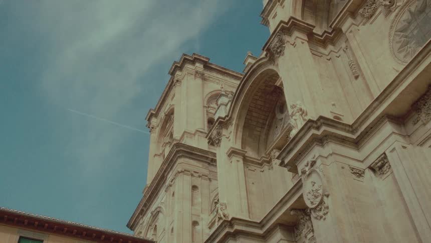 A low angle shot shows the ornate stone facade of a historic cathedral against a blue sky