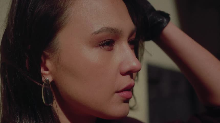 A stylish woman in a black leather glove lowers her hand from her face in a dramatic, cinematic slow-motion close-up