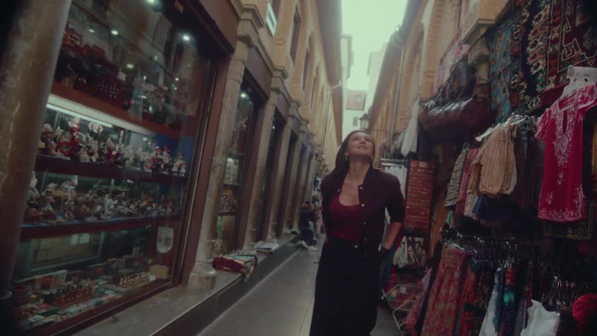 A woman takes in the sights of a narrow, historic marketplace, browsing the vibrant clothing and souvenir stalls