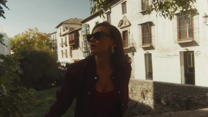 A chic woman wearing sunglasses pauses on a sunny street, taking in the sights of a historic European city