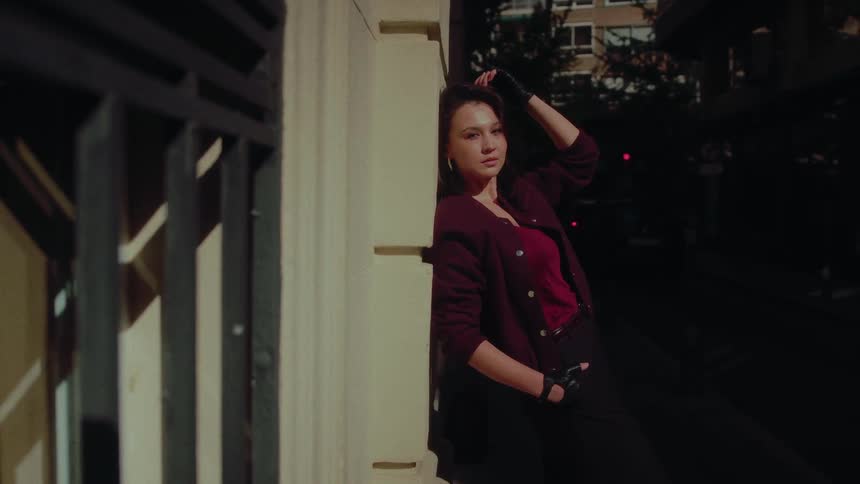 A stylish and pensive woman leans against a city wall at night, bathed in warm, dramatic light