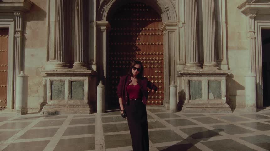 A stylish woman stands confidently in front of a grand, historic European building on a sunny day