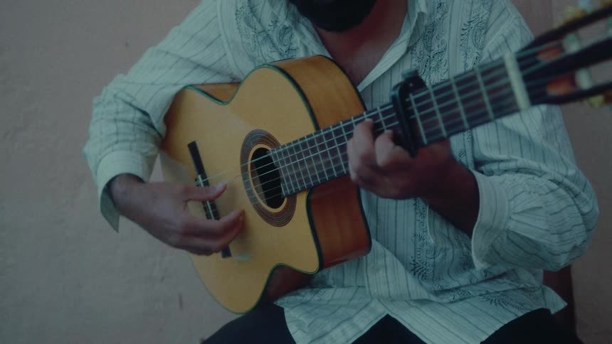 A talented musician with a beard passionately strums and fingerpicks a Spanish-style melody on his classical acoustic guitar