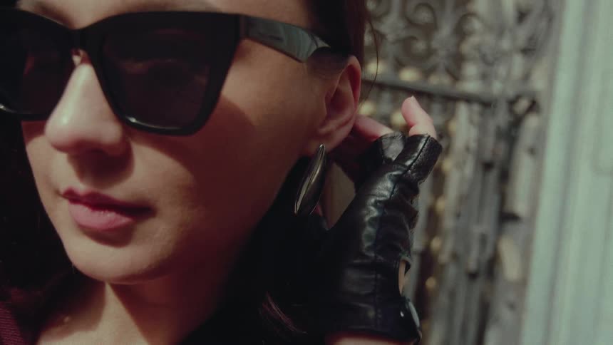 Stylish woman wearing sunglasses and fingerless leather gloves adjusts her hair and earring in slow motion
