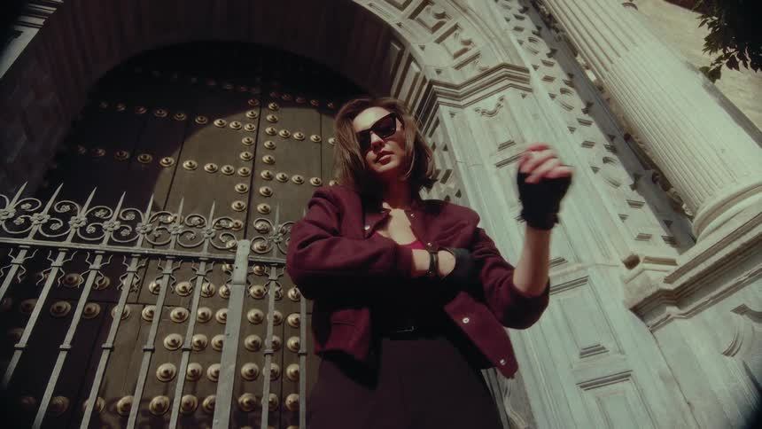 Low angle shot of a stylish woman in sunglasses and fingerless gloves posing powerfully in front of an ornate door