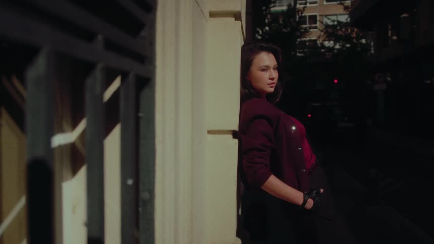 Cinematic slow-motion shot of a stylish woman posing against a sun-drenched wall on a city street