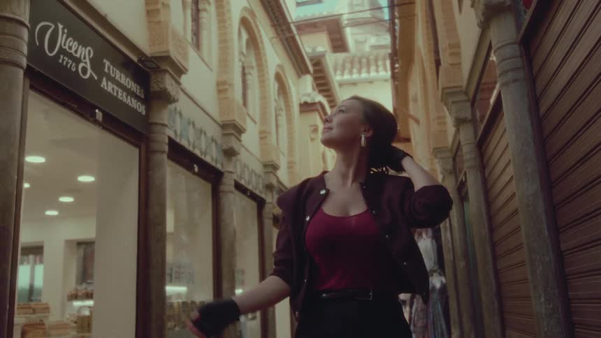 A stylish young woman gracefully walks through a charming narrow European alleyway, pausing to admire the architecture