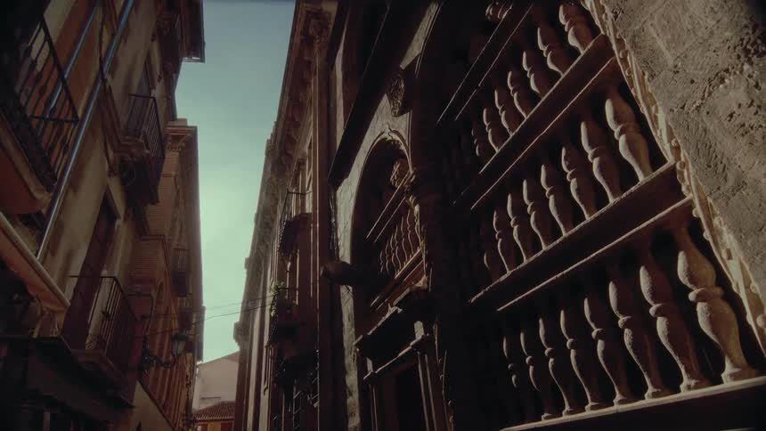 A slow zoom captures the dramatic sunlight and shadows on an ornate stone building in a narrow historic alleyway