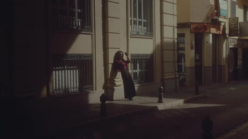 A stylish woman poses dramatically in a spotlight on a quiet European street corner at night