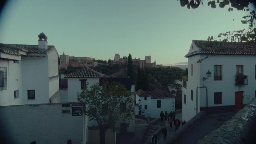 A scenic view of the Alhambra palace in Granada, Spain, from a winding street at dusk