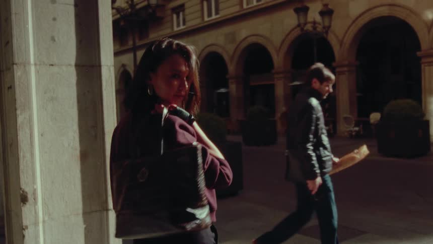 A stylish woman looks over her shoulder in slow motion while standing in a sunlit European arcade