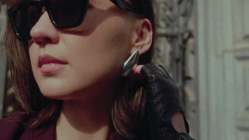 A chic woman wearing sunglasses and fingerless leather gloves adjusts her hair in slow motion