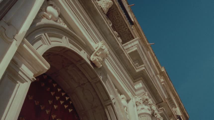 A static low-angle shot reveals the intricate, classical architecture of a historic building against a clear blue sky