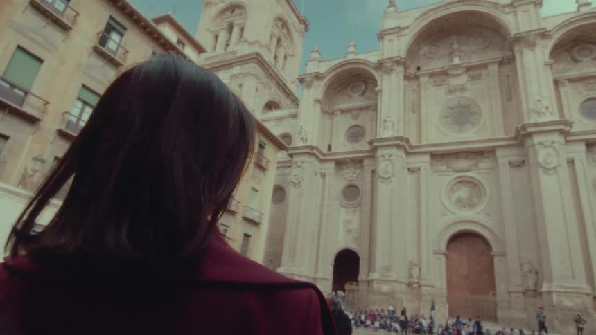 A beautiful woman removes her sunglasses in slow motion as she gazes up in awe at a magnificent historic cathedral in a European city square
