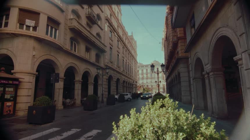 A nostalgic, vintage film shot of a quiet street lined with classic European architecture on a sunny day