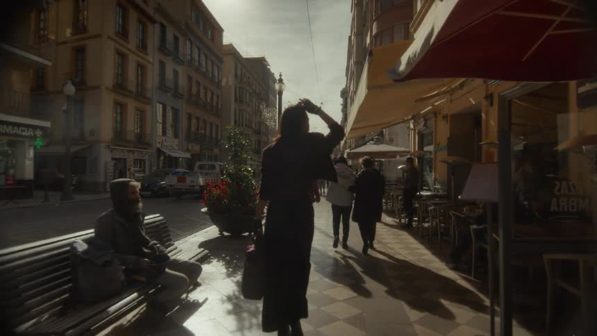 A slow-motion follow shot captures a woman walking down a sunlit street in a historic European city