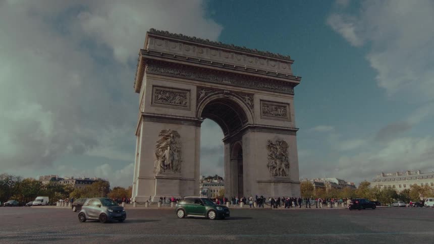 A wide shot captures the majestic Arc de Triomphe in Paris as city traffic flows around the historic monument