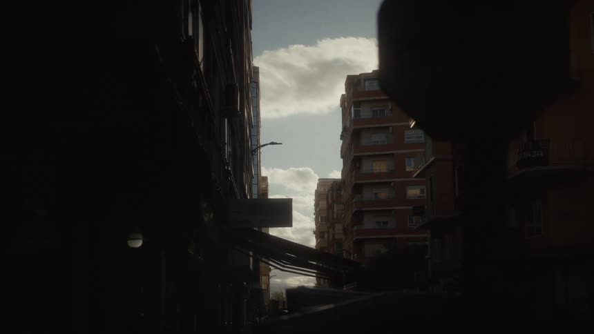 Time-lapse of clouds passing over a sunny sky framed by silhouetted city buildings on an urban street