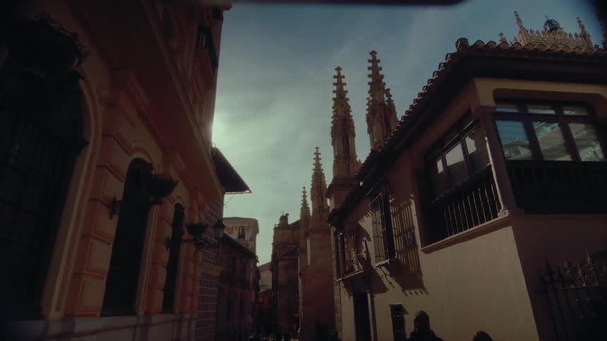 Spires of a historic Gothic cathedral tower over a sunlit narrow street in an old European city