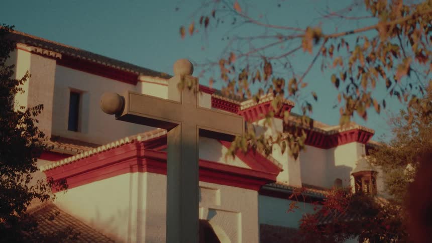 A stone cross stands in the foreground of a beautiful Spanish-style church during the golden hour