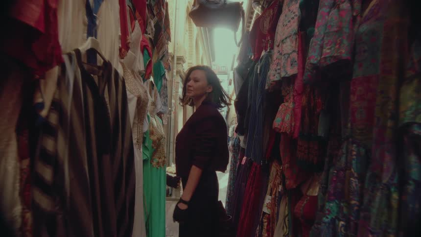 A stylish woman walks through a narrow alley in an exotic market stall and turns to smile warmly at the camera in slow motion