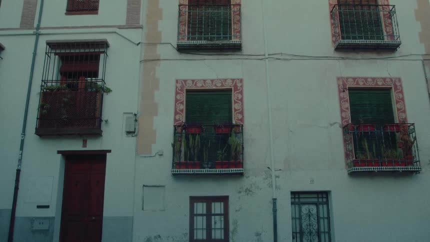 Static shot of a weathered building facade with ornate balconies and windows on a quiet street