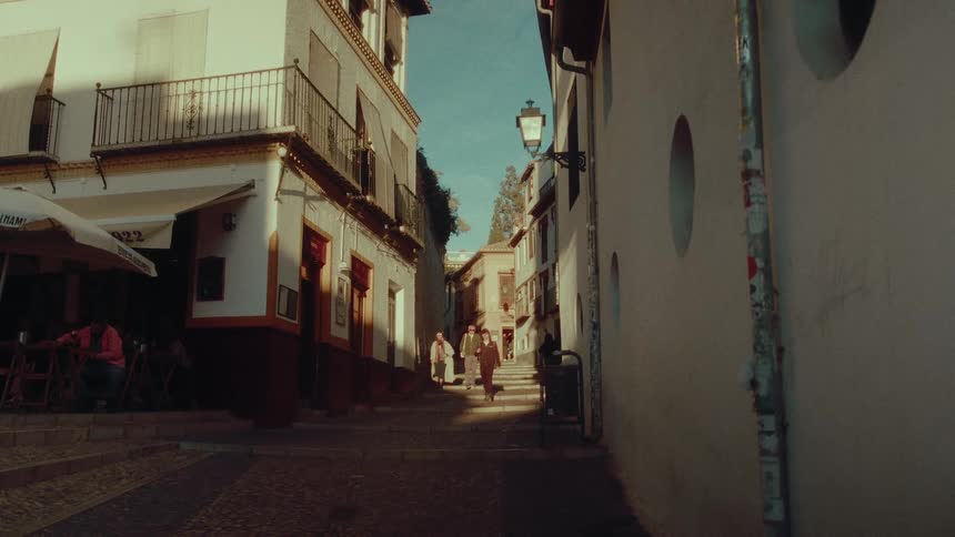 A static view of a sunlit cobblestone alley in a historic European city with people walking in the distance
