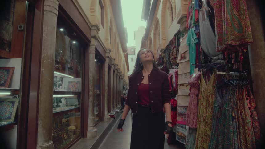 A woman walks down a narrow, vibrant market alley, admiring the shops and clothing in slow motion