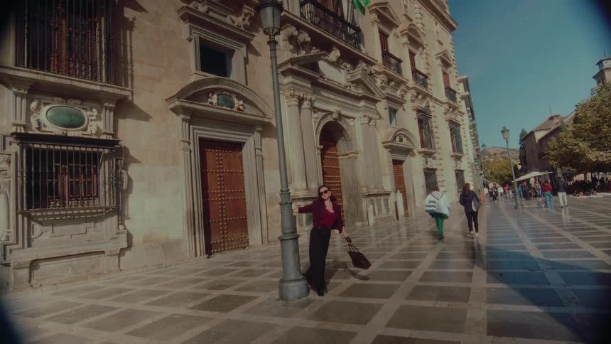 A stylish woman strikes a pose next to a lamppost in a historic Spanish plaza on a sunny day
