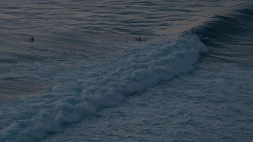 A surfer rides a long, rolling ocean wave in slow motion during the quiet twilight hours