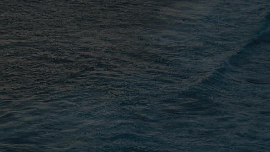 A meditative and abstract top-down shot of dark, deep ocean water gently rolling in slow motion