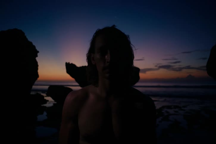 Mysterious man's face illuminated by a flashing light against a colorful sunset on the beach