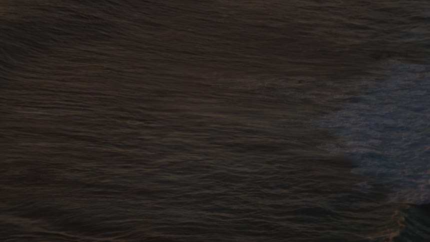 An overhead slow motion shot shows a dark ocean wave cresting and breaking into white foam under the golden light of sunset