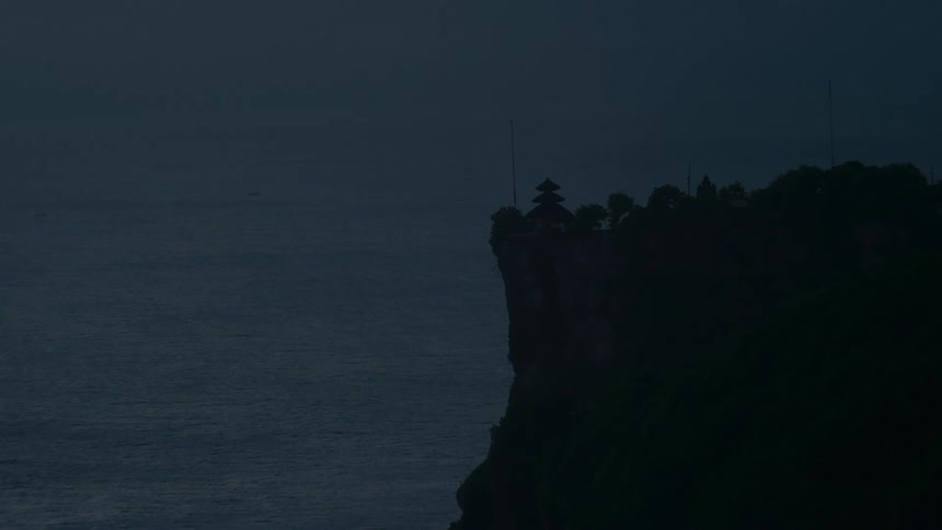 A mysterious view of a silhouetted temple perched atop a dark cliff overlooking the vast, calm ocean at dusk