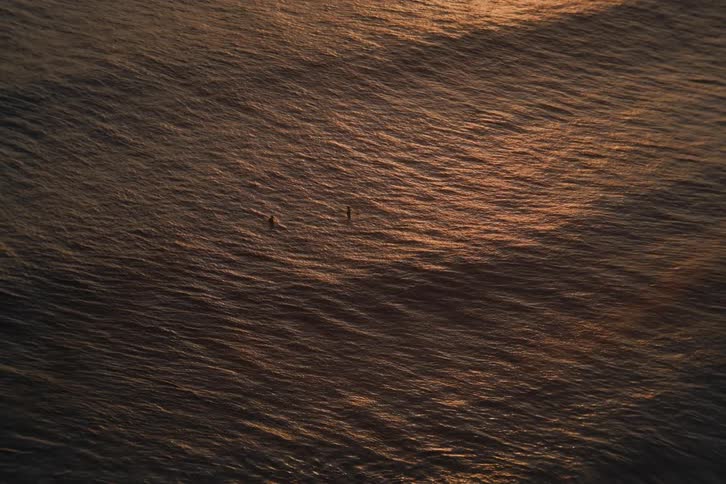 Two distant surfers float peacefully in the vast golden ocean at sunset
